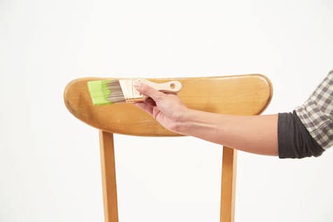 Hand holding paint brush over chair